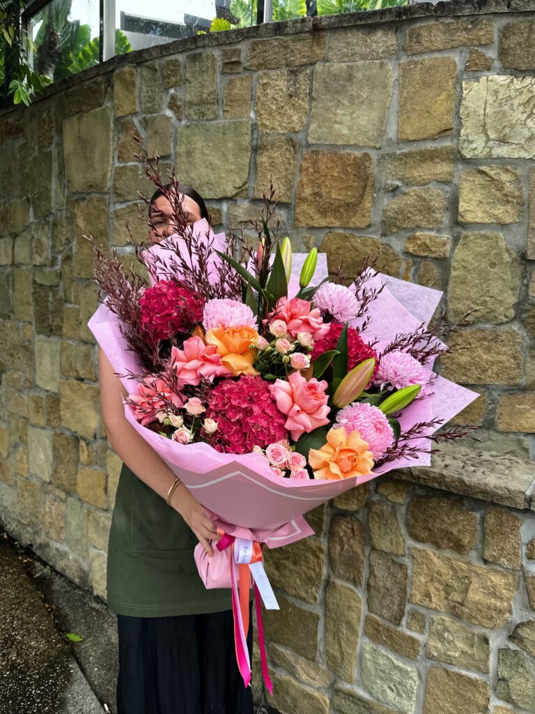 Large pink and peach floral bouquet featuring hydrangea, roses and chrysanthemums wrapped in pink paper