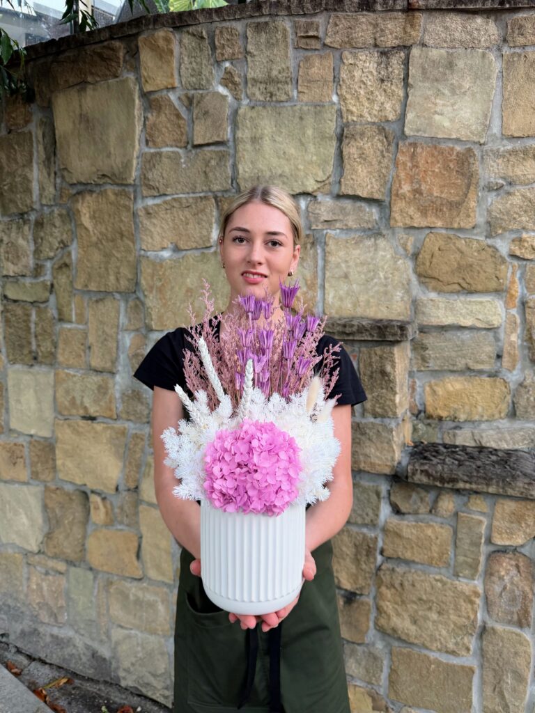 Lilac Whisper dried and preserved flower arrangement featuring pink hydrangea, lilac preserved flowers and white foliage in a white ceramic vase.