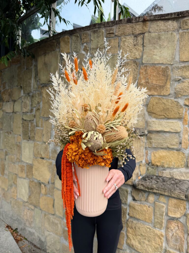Amber Harvest dried and preserved flower arrangement with orange hydrangea, cream foliage, banksia and cascading orange amaranthus in a ribbed neutral vase.