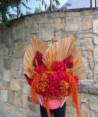 Sunset Sangria dried and preserved flower arrangement with pink and orange hydrangea, dried palm leaves and cascading orange amaranthus in a ribbed pink vase.