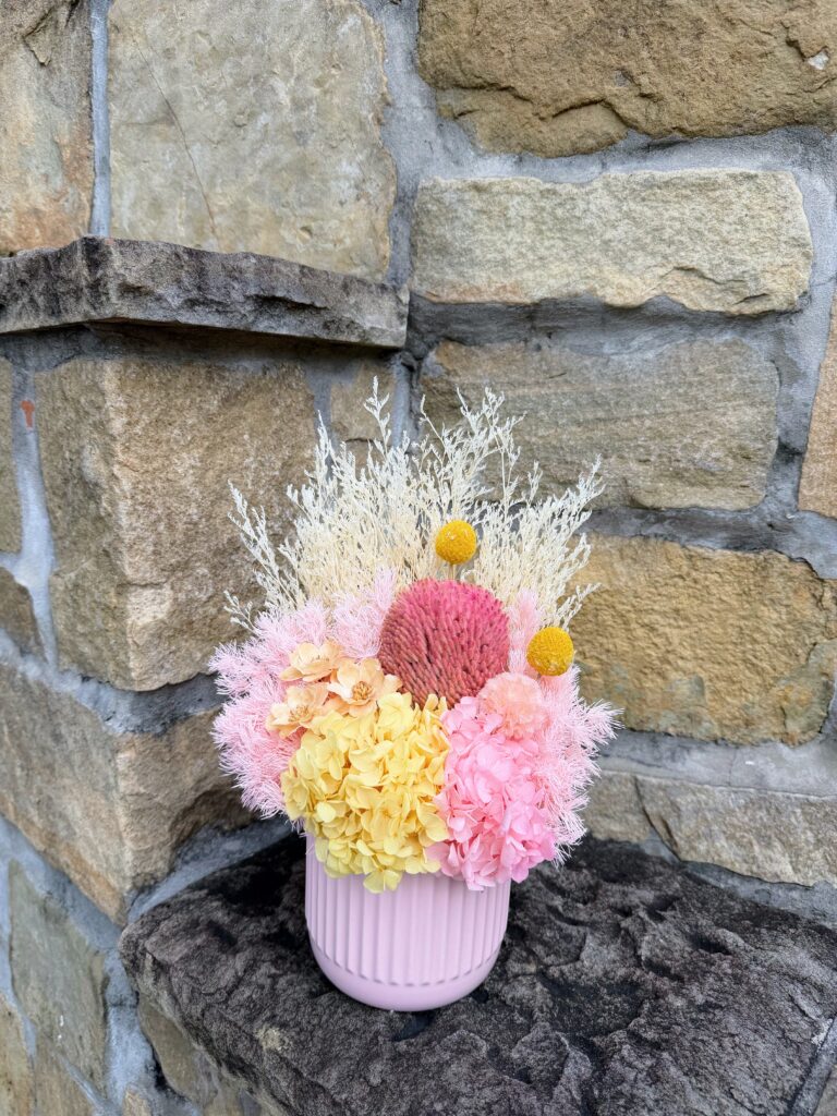 Sherbet Dreams dried and preserved flower arrangement with pink and yellow hydrangea, pink banksia and yellow billy buttons in a ribbed pink vase.