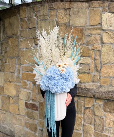 Blue Lagoon dried and preserved flower arrangement with blue hydrangea, white foliage and cascading blue amaranthus in a ribbed white vase.