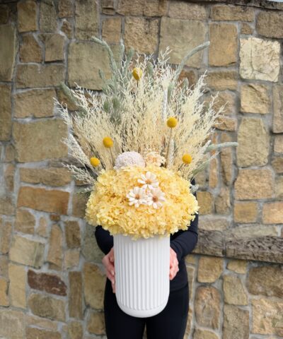 Golden Meadow dried and preserved flower arrangement in yellow, cream and sage tones, presented in a white ribbed vase.
