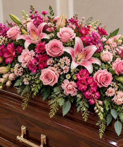 Forever Blooming Love pink funeral casket spray featuring pink roses, pink lilies, vibrant fuchsia flowers and cascading greenery.