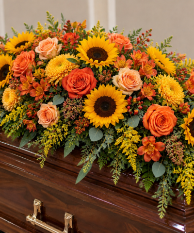A Life Full of Sunshine casket spray featuring yellow sunflowers, orange roses, golden chrysanthemums, orange alstroemeria and greenery on a coffin.