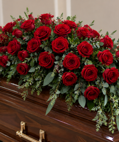 Forever in My Heart Casket Spray featuring deep red roses and cascading eucalyptus greenery on a wooden coffin